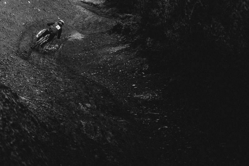 A mountain biker dropping into a dark forest trail