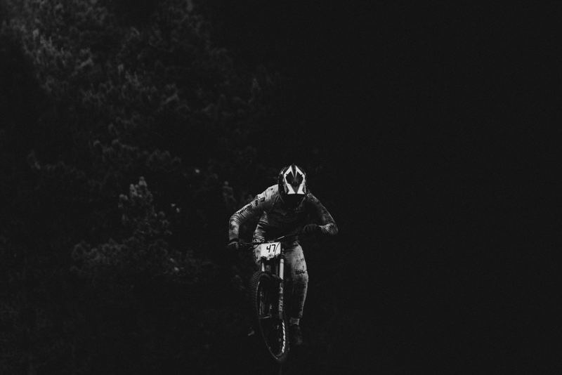 A downhill rider mid-jump against a dark treeline