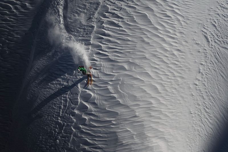 A snowboarder cutting a line down a wind-rippled face