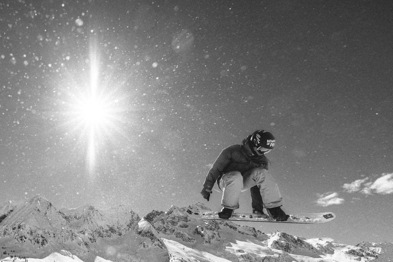 A snowboarder on a summit ridge with the sun flaring
