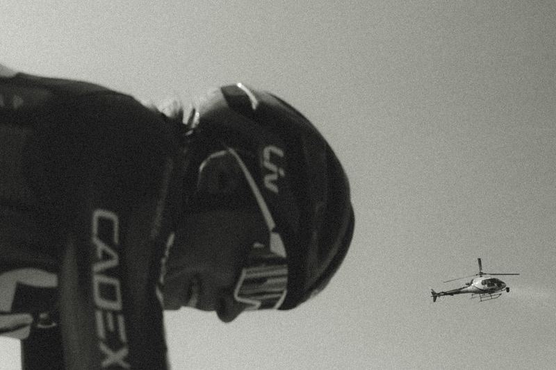 A road cyclist seen from below against the sky, a helicopter following