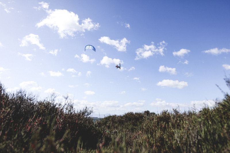 A kitesurfer high above the scrub, kite against a bright blue sky