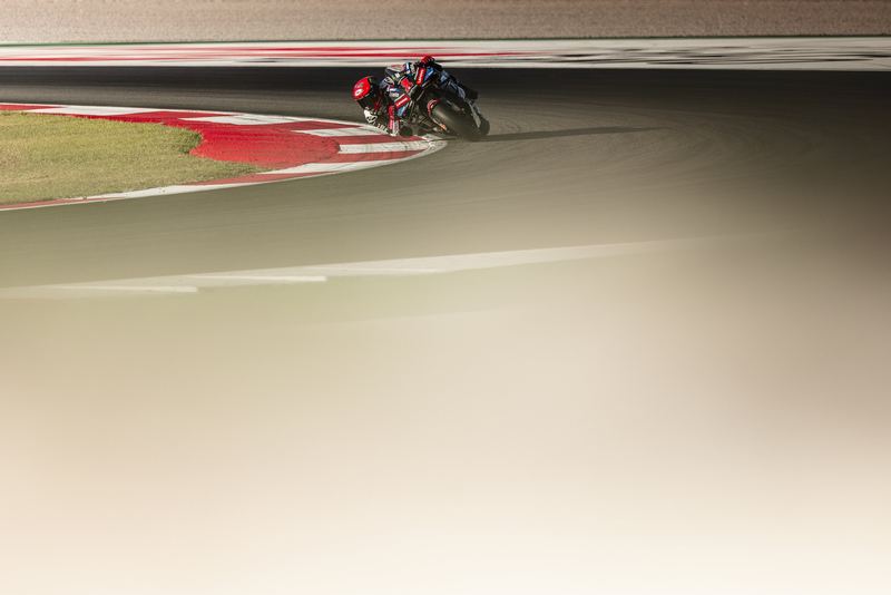 A Ducati MotoGP bike leaning through a corner over heat-hazed asphalt