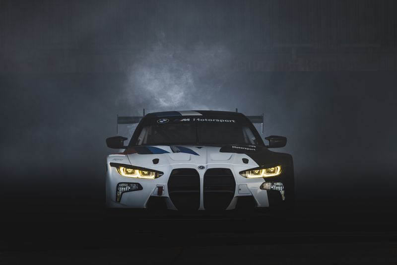 A BMW M4 GT race car emerging from smoke in a dark studio