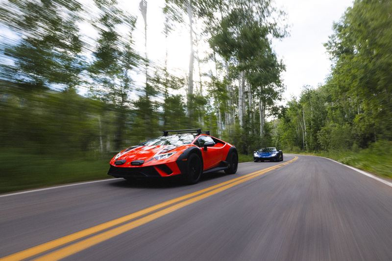 An orange sports car panned along a tree-lined road