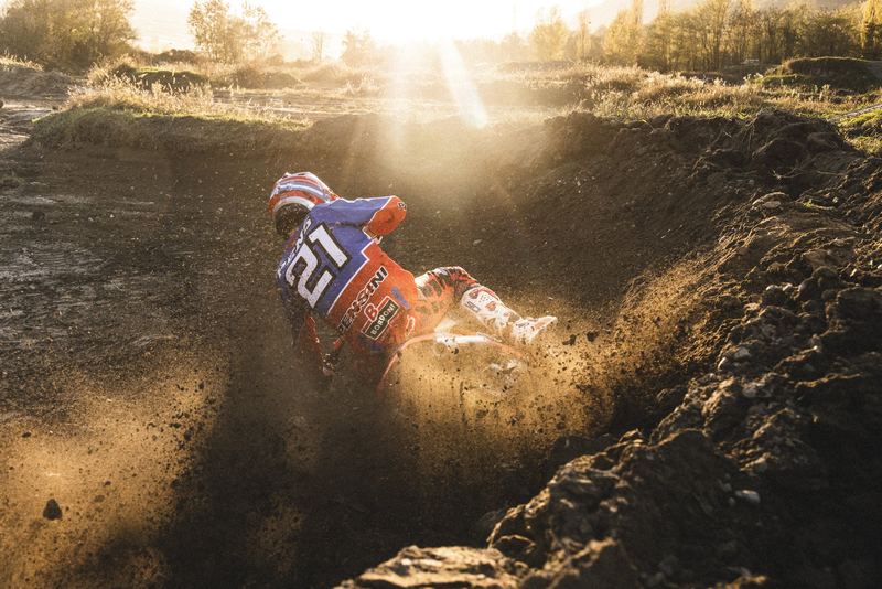 A motocross rider deep in a dirt rut, sun flaring behind