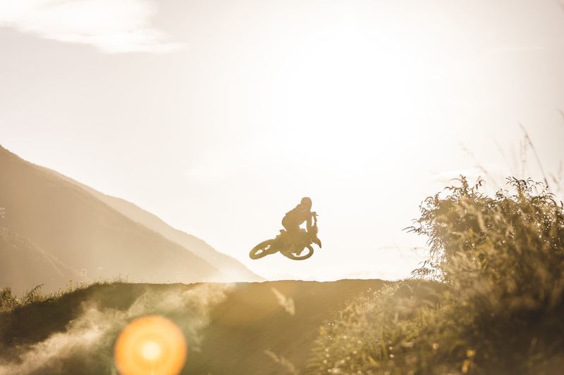 A motorcycle silhouetted on a hill crest against the low sun
