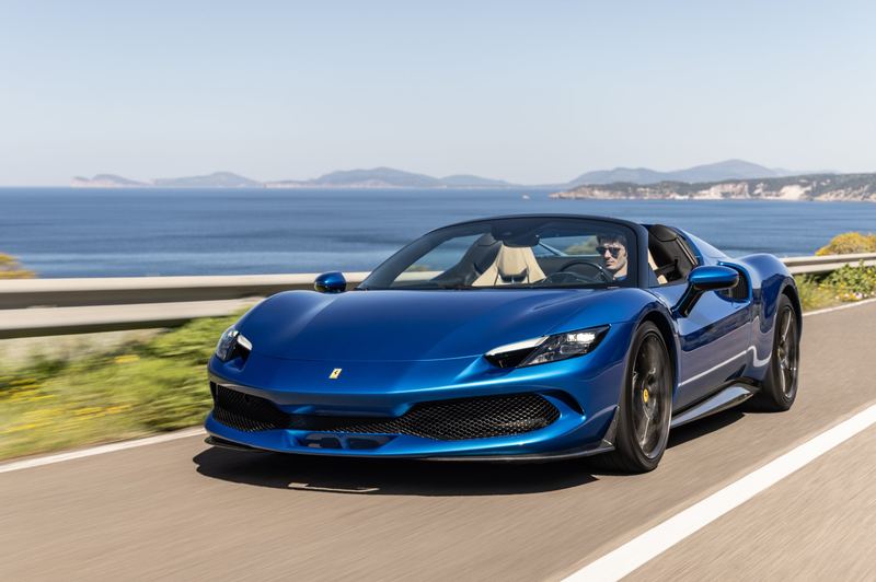 A blue Ferrari Spider on a coast road above the sea