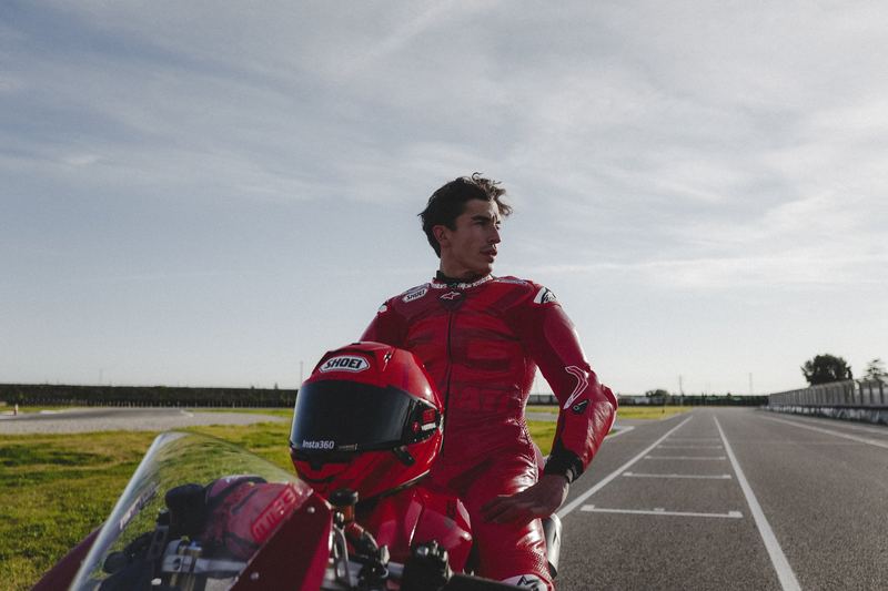 A racer in red leathers standing over the bike on a wet track