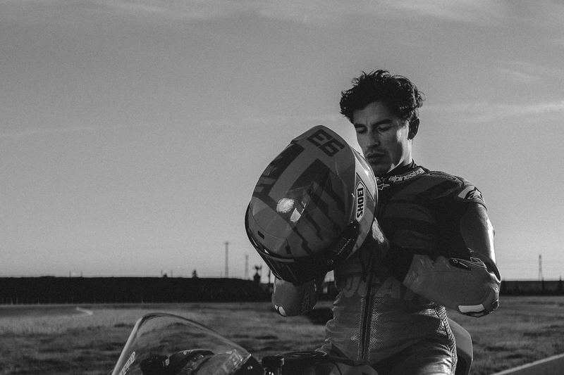 A rider holding his helmet, sea and sky behind