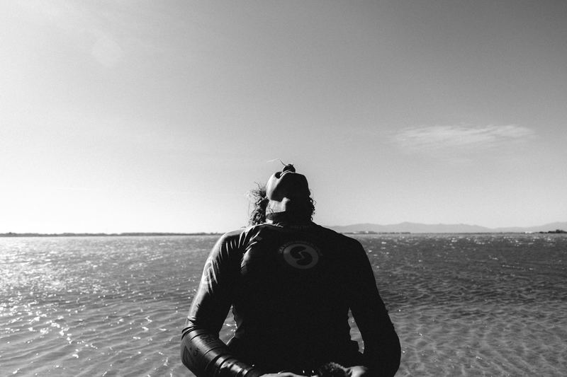A wetsuited figure standing on a flat, empty beach